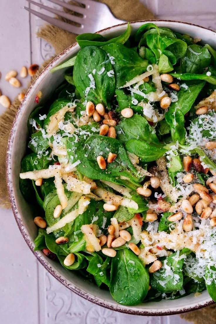 Feldsalat mit Äpfeln, Parmesan und Pinienkernen auf einem Teller serviert.