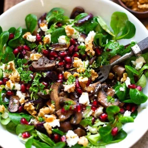 Frisch zubereiteter Feldsalat mit gebratenen Pilzen, Granatapfel, Feta und Walnüssen