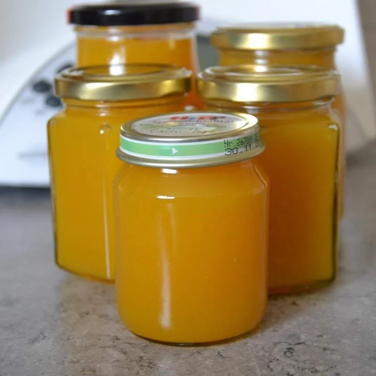 Glas mit selbstgemachter Mango-Pfirsich-Marmelade auf Holztablett