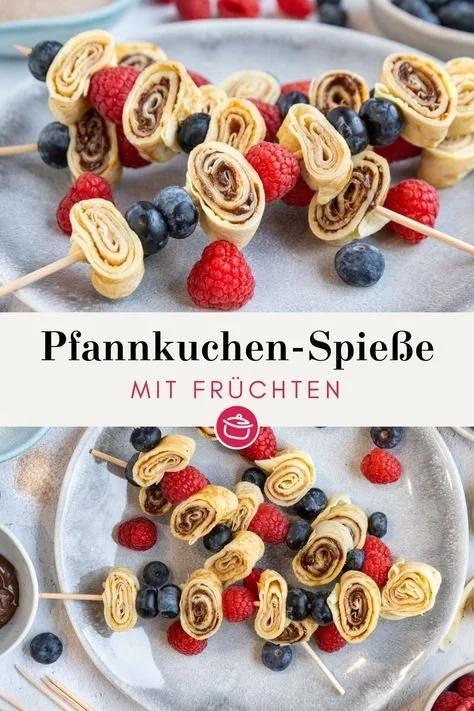 Bunte Pfannkuchen-Spieße auf einem Teller, verziert mit Obst und Schokolade.