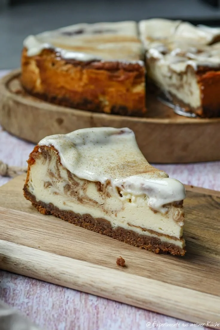 Zimtschnecken-Cheesecake auf einem Teller, dekoriert mit Zimt und Sahne