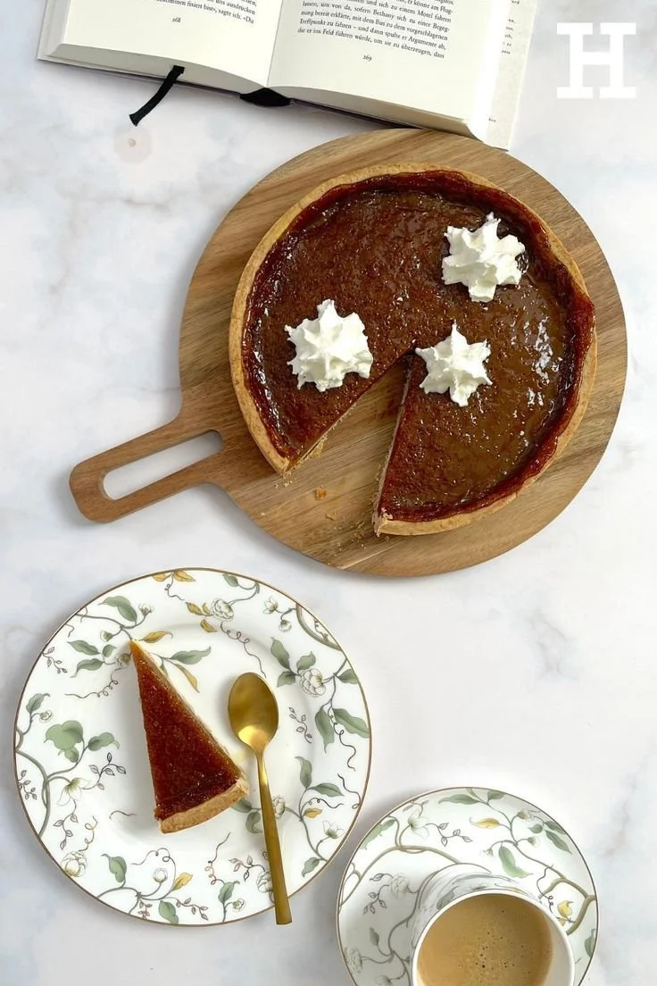 Veganer Pumpkin Pie auf einem Teller mit frischen Kürbissen im Hintergrund